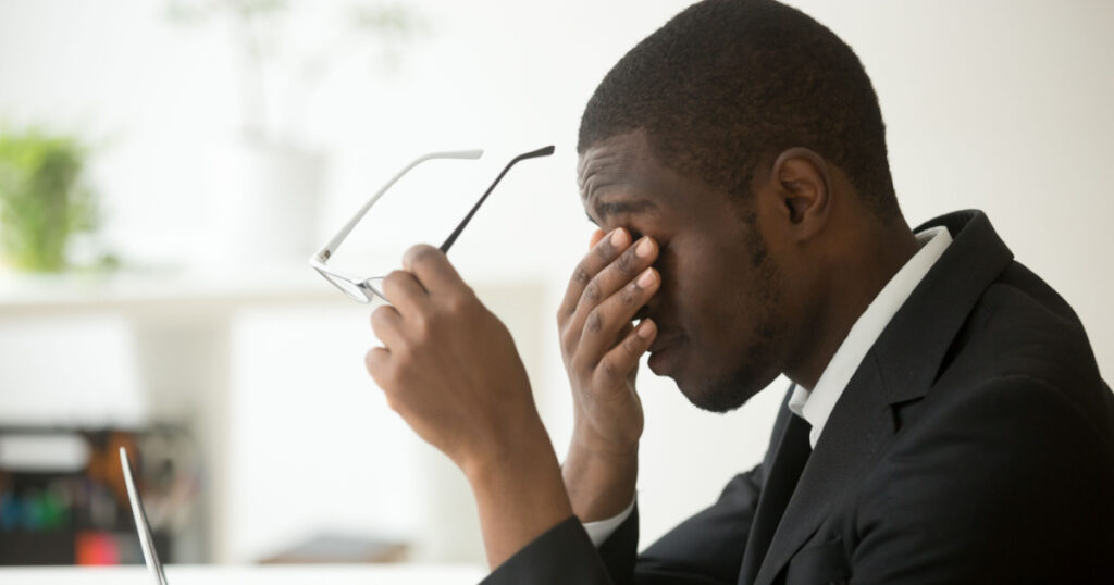 Tired of computer african businessman taking off glasses feels eye strain fatigue after long office work on laptop, exhausted overworked stressed depressed black man having bad sight vision problem 