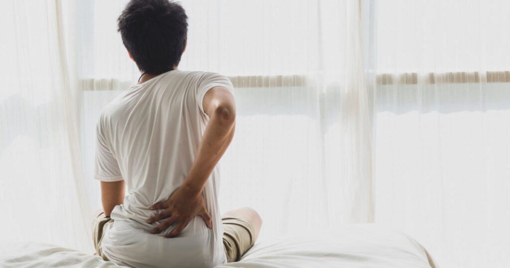 man back pain and sit on bed in bedroom