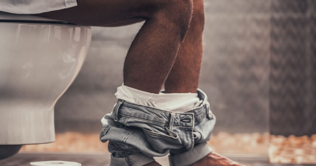 Man Sitting on Toilet in Bathroom