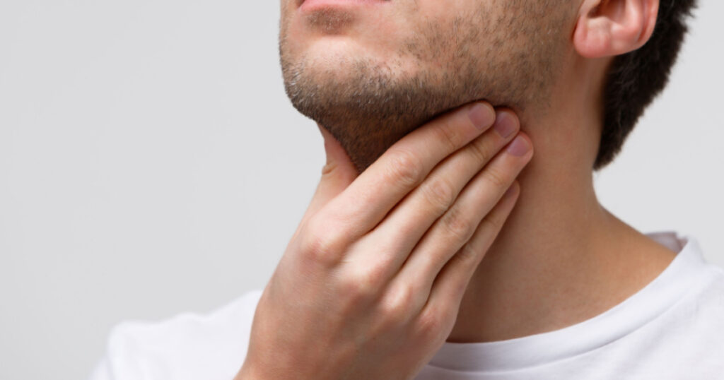 Close up of sick man suffering from throat problems, grey background, isolated. Thyroid gland, painful swallowing, pharyngitis, laryngeal swelling concept. Inflammation of the upper respiratory tract